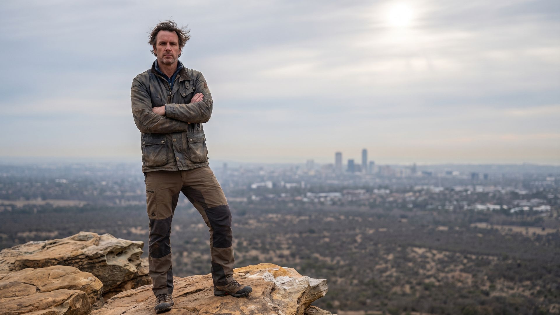 A man standing grounded on a rocky outcrop in the Colorado foothills with Denver far below